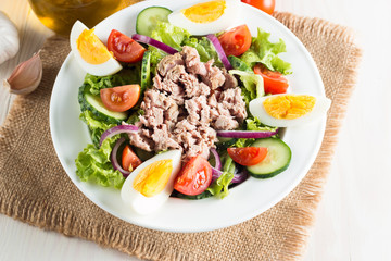 Fresh fish tuna salad made of tomato, ruccola, tuna, eggs, arugula, crackers and spices. Caesar salad in a white bowl on wooden background