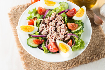 Fresh fish tuna salad made of tomato, ruccola, tuna, eggs, arugula, crackers and spices. Caesar salad in a white bowl on wooden background