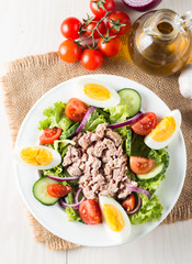 Fresh fish tuna salad made of tomato, ruccola, tuna, eggs, arugula, crackers and spices. Caesar salad in a white bowl on wooden background