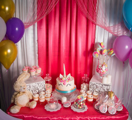Sweet table and big unicorn cake for baby girl first birthday. Candy bar with a lot of different candies and sweet cakes