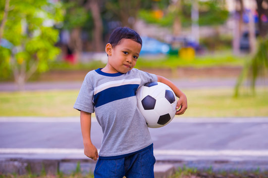 Outdoors Portrait Of 5 Or 6 Years Old Young Asian Indonesian Kid Posing Happy With Soccer Ball Playing Football In Child Sport Practice Education Isolated On Urban Park