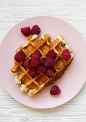 Traditional belgian waffle with raspberries on pink plate on white wooden table, top view. Flat lay, overhead, from above. Close-up.