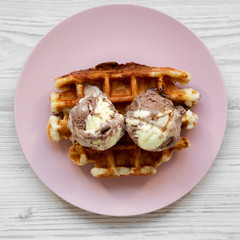 Traditional belgian waffle with icecream on pink plate on a white wooden table, top view. Closeup.