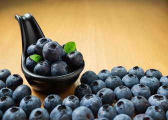 Pile of blueberries in black spoon on wood table background