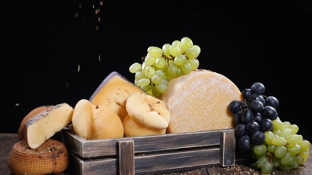 Set of hard cheese beautifully put in wooden box decorated with grapes. Spices falling down on composition in slow motion. Restaurant showroom. Food art. hd