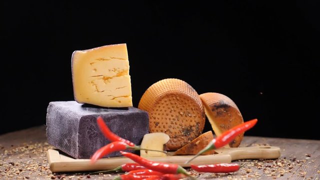 Food video. Luxury food concept. Cheese restaurant serving. Food art concept. Variety of hard cheese put on wooden board. Pods of red pepper falling down in slow motion. hd