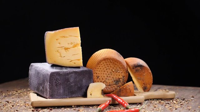 Food video. Luxury food concept. Cheese restaurant serving. Food art concept. Variety of hard cheese put on wooden board. Pods of red pepper falling down in slow motion. hd