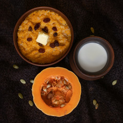 Rice porridge cooked in milk with pumpkin, millet, butter, raisins, banana and nuts, served in pottery, on a dark knitted background
