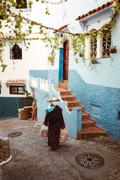 Frau tragt einen traditionellen Hut und geht durch eine Gasse in Chefchaouen der blauen Stadt in Marokko