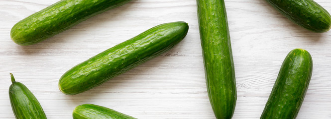 Fresh organic green cucumbers on white wooden surface, overhead view. Flat lay, from above, top view.
