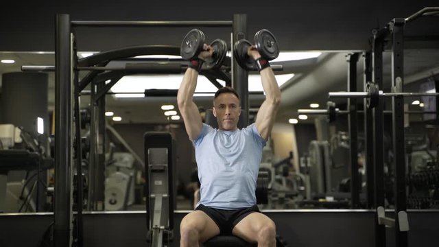 Muscular man holding dumbbell above the head at the gym.