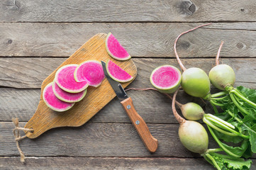 Sliced watermelon radish (chinese daikon) with green leaves on wooden table. Top view.