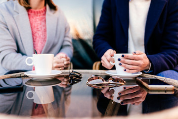 people, communication and friendship concept - smiling young women drinking coffee or tea and talking at outdoor terrace cafe