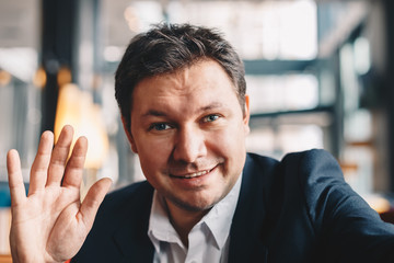 Close-up of attractive young man having a business conference video call in a cafe bar, smiling and...