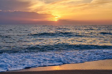 Tropical beach. Colorful sunset seascape. Waves with foam hitting sand.