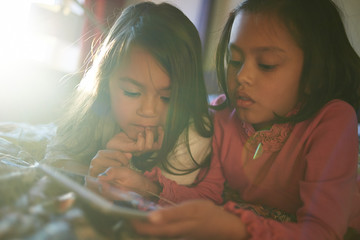 Two cute young Asian sisters lying on the bed playing together with a mobile device 