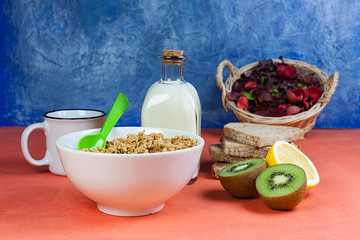 DESAYUNO CON TAZÓN DE CEREALES MUESLI , KIWI, LIMON,PAN RÚSTICO, BOTELLA DE LECHE JUNTO A CESTA CON FLORES SECAS