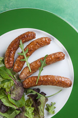 PRIMER PLANO DE PLATO DE SALCHICHAS CON ENSALADA SOBRE PLATO BLANCO Y VERDE