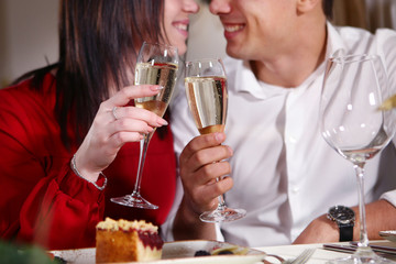 Couple in love: a girl and a young man in a restaurant holding glasses of champagne. Hands close-up, faces out of focus. The concept of holiday, love, Valentine's day