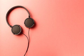 Minimalistic top view composition with black headphones on coral background with a lot of copy space for your text. Close up, flat lay. Living Coral color of the Year 2019. Music concept