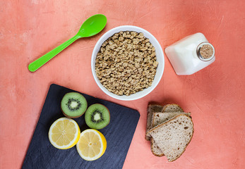 VISTA CENITAL DE DESAYUNO CON CEREALES MUESLI, KIWI, LIMON, PAN RÚSTICO Y BOTELLA DE CRISTAL CON LECHE