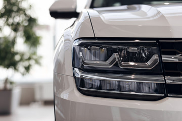 Closeup headlights of a modern white color car. Detail on the front light of a car. Modern and expensive car concept. The car is in the showroom