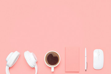 Trendy flat lay mockup with headphones, diary, pen, wireless mouse and cup of coffee on coral colored desk. Top view. Modern feminine workspace.