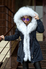 Obraz premium a girl in a black jacket with a white fur collar and glasses posing on the street