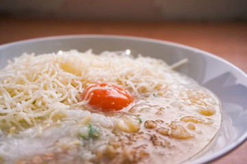 rice porridge in thai style or congee with egg, pork in a white bowl on wood table 