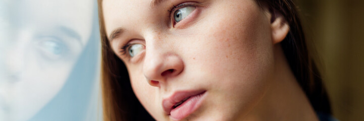Young depressed lonely female college student standing by a window at her school, looking out....