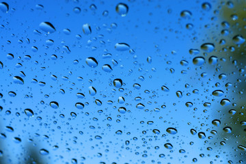 Large drops of water on transparent glass after a rain, reflection of trees in drops, a bright blue background
