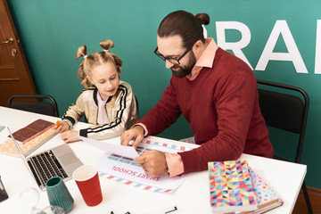 Fototapeta premium Dark-haired bearded smiling teacher showing pictures to his pupil