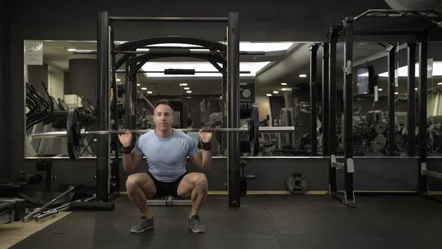 Image of a muscular man doing squads with heavy barbell at the gym.