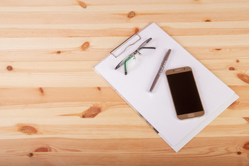 Pusty notatnik z okularami, długopisem i telefonem na drewnianym biurku.