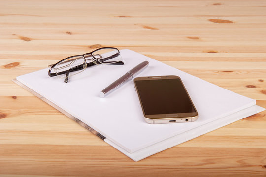 Pusty notatnik z okularami, długopisem i telefonem na drewnianym biurku.