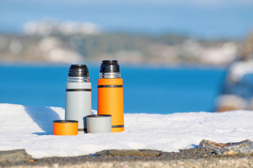Thermos with hot tea on a snowy sea coast