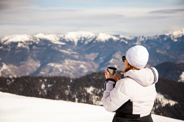Adult woman with thermos on mount top with spectacular view of snowy mountains on background