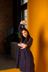 brunette girl, regular student, teenager, posing for a photo in a photo studio on a yellow background dressed in a casual blue dress for every day