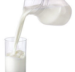 Pouring milk from jug into glass isolated on white background