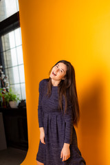 brunette girl, regular student, teenager, posing for a photo in a photo studio on a yellow background dressed in a casual blue dress for every day