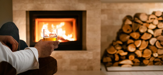 Man sitting at home by the fireplace and drinking a whiskey.  