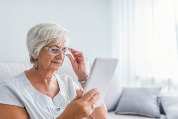 Fototapeta premium Senior woman with tablet sitting on couch in living room