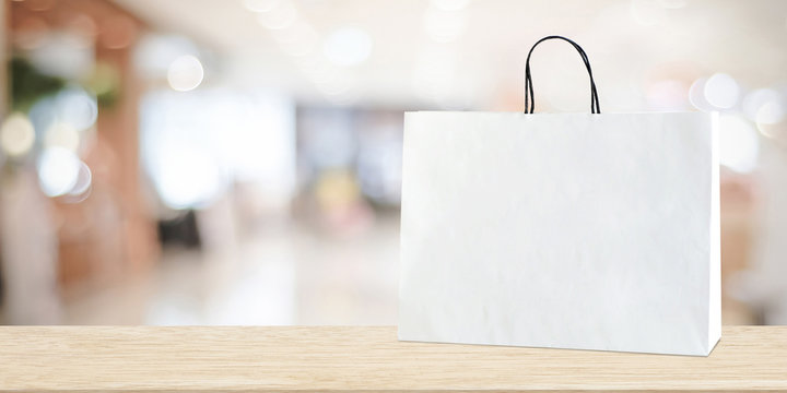 White shopping bag on wooden table over blurred store background, business, template, product display montage background