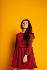 Naklejka premium Attractive, Slim, Beautiful, Brunette Girl Wearing Red Silk Fabric Dress Fly And Wave In The Wind Posing in Studio on Yellow background. Spring colletcion concept