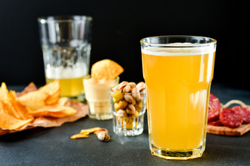 two glasses of beer and snacks chips, nachos with sauce, pistachios and salami, aperitif, relax in the bar with friends, beer party.  selective focus and copy space