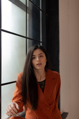 portrait of an attractive sexy girl dressed in a stylish suit sitting on the window sill near a large window