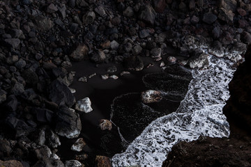 Fototapeta premium Wellen treffen auf Schwarzsand und schäumen auf