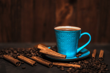 Cup of aromatic black coffee, coffee beans and cinnamon sticks on dark background. Still life.