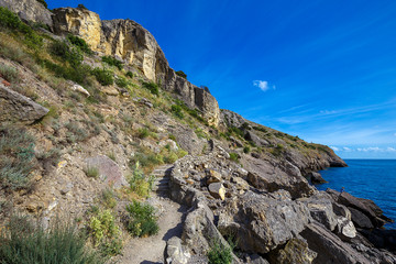 Naklejka premium Stone trail with steps through rocky mountains overgrown green trees with view clear azure water of sea at sunny day on background beautiful blue sky. Beautiful sea landscape.
