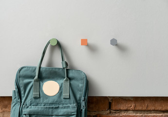 Metal multicolored geometric hangers with hanging casual bag on light wall in studio